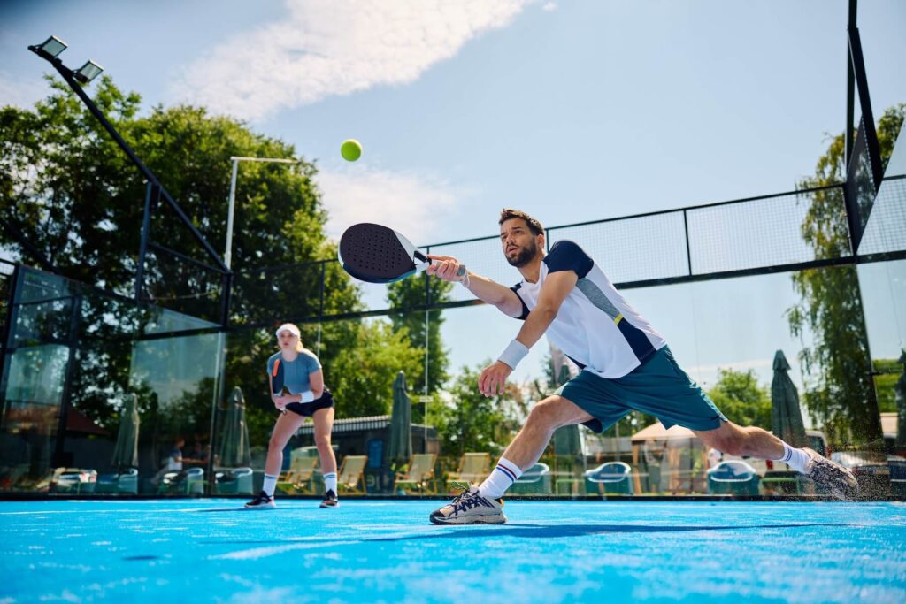Padel doubles match showing gameplay with glass walls at outdoor court in Utah County