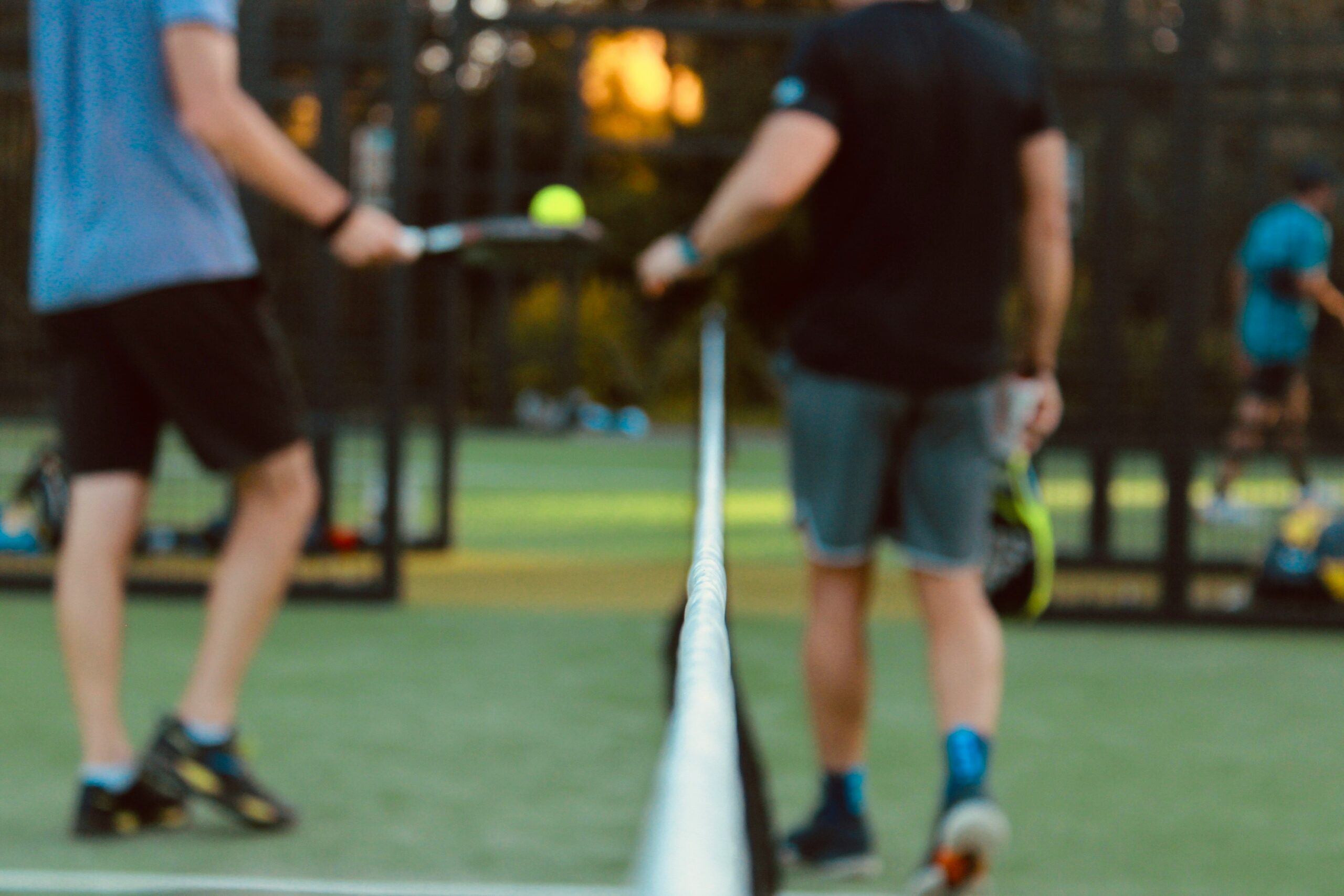 Two padel tennis players holding rackets on opposite sides of the net during a casual evening game, showcasing the social doubles format and community atmosphere of padel in Utah with golden hour lighting on artificial turf court