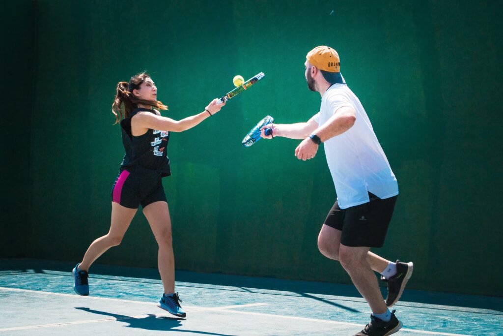 A man and a woman in athletic wear playing a doubles match of Padel on an outdoor green court in Orem.
