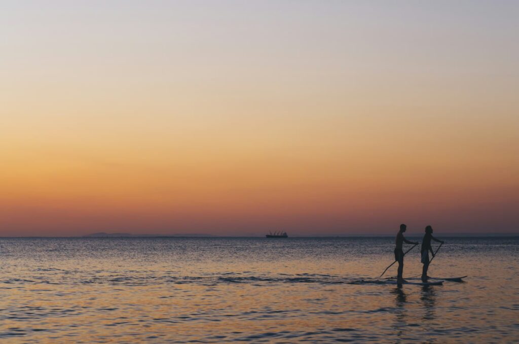 Silhouettes of a couple stand-up paddleboarding together on a calm lake in Utah County during a vibrant orange sunset.
