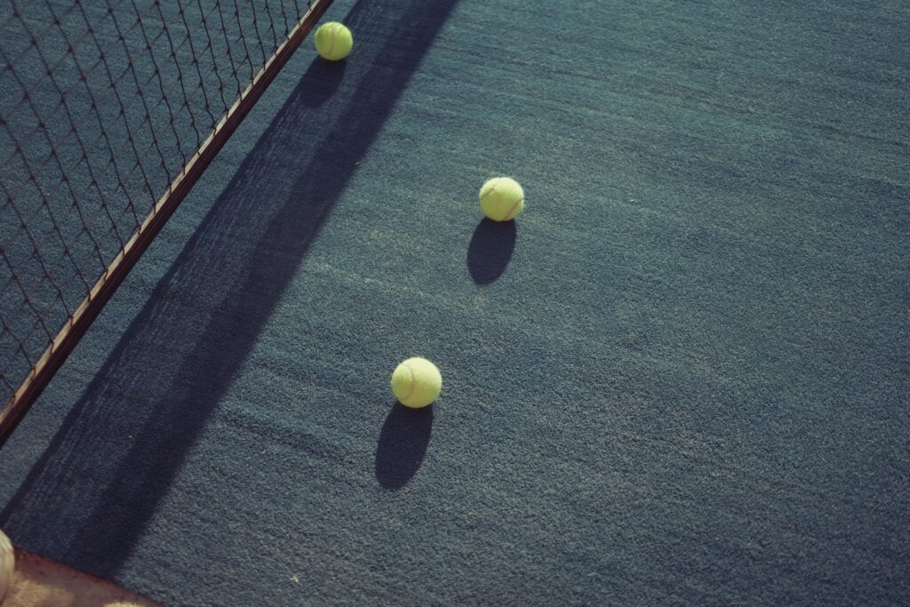 Three yellow padel tennis balls lying on the blue turf near the net.
