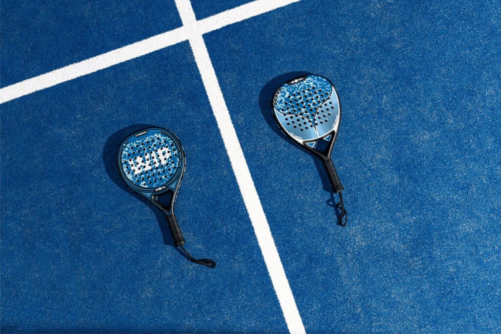 Two blue round-shaped padel rackets lying crosswise on a blue court with white boundary lines.