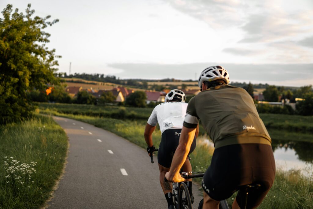 Two cyclists riding on a paved trail at sunset, showcasing cycling as a top tier choice among low impact sports for leg strength and heart health.