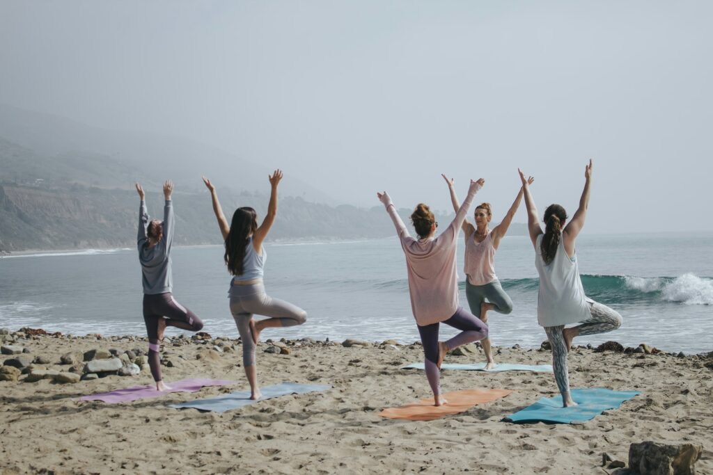 A group of people practicing yoga on the beach in tree pose, demonstrating low impact sports for better balance and mobility.