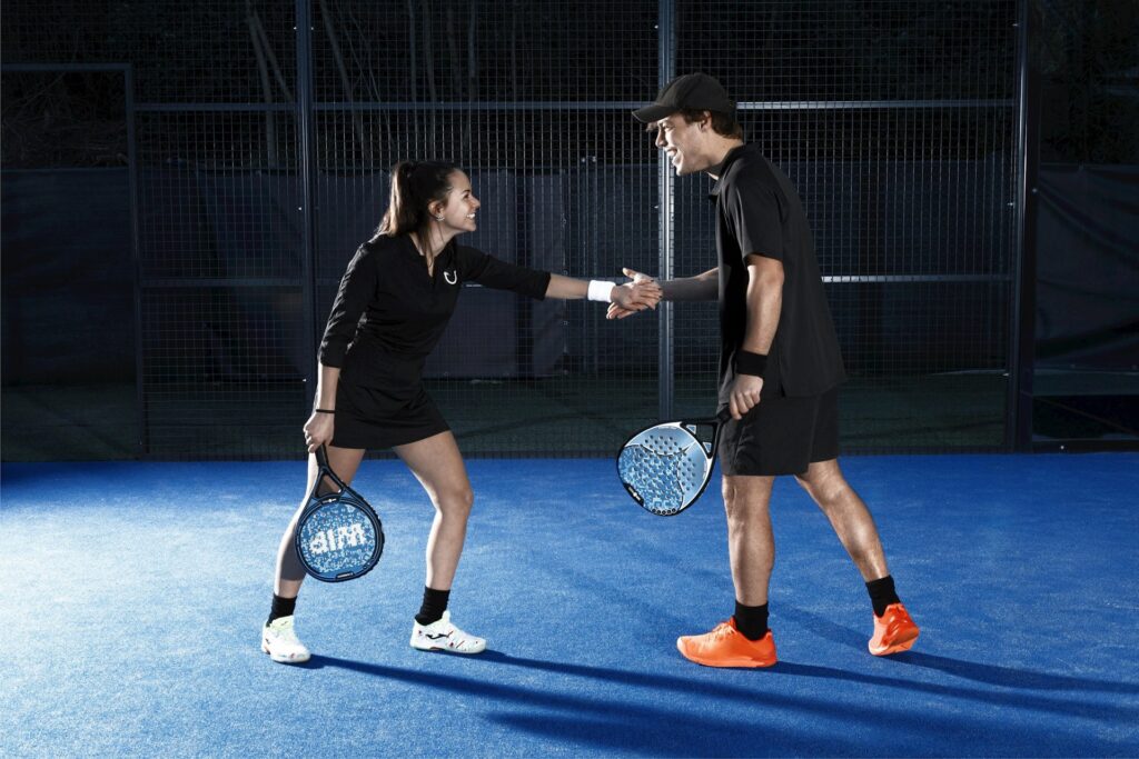 A man and woman smiling and shaking hands on a blue indoor padel court, representing fun indoor activities in Utah County.