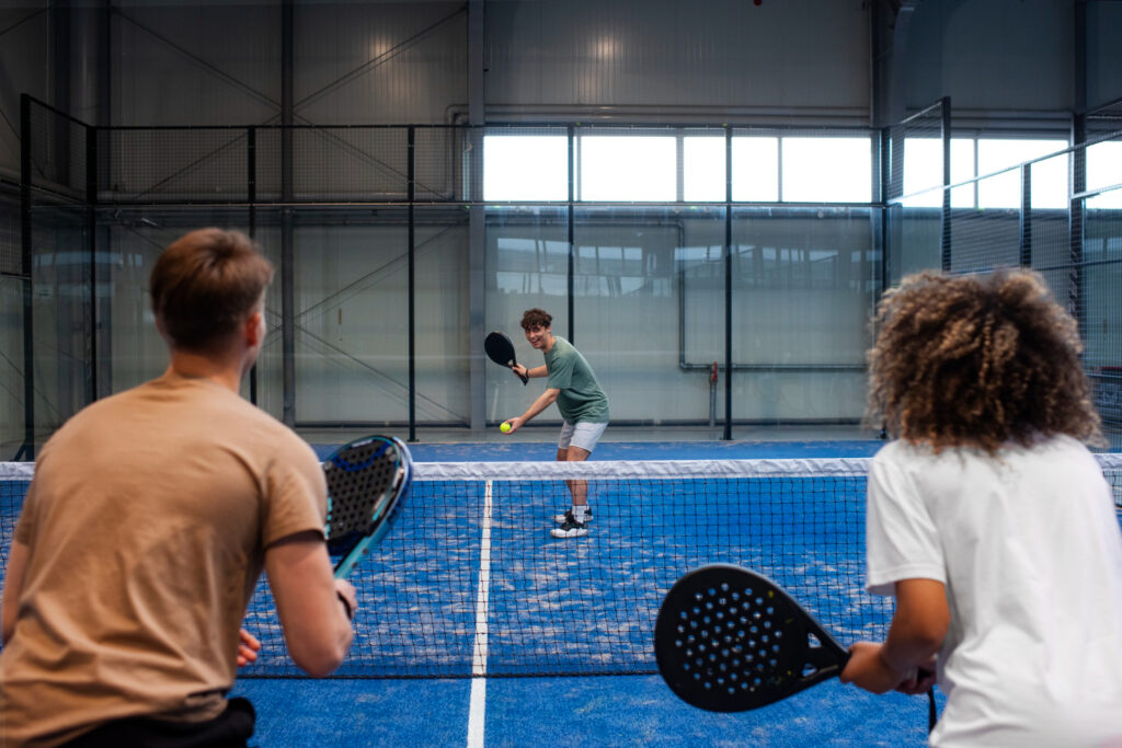 Four players competing in an indoor doubles match, illustrating proper team net positioning and padel strategy.