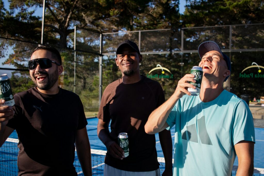 A group of friends laughing and socializing on a blue court after playing a fun match of padel tennis.