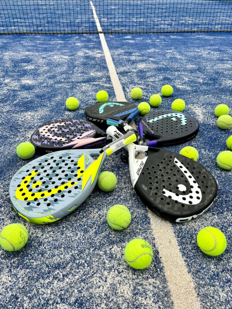 Four premium padel rackets and yellow balls resting on the blue indoor turf, available for rent to play padel in Utah County.