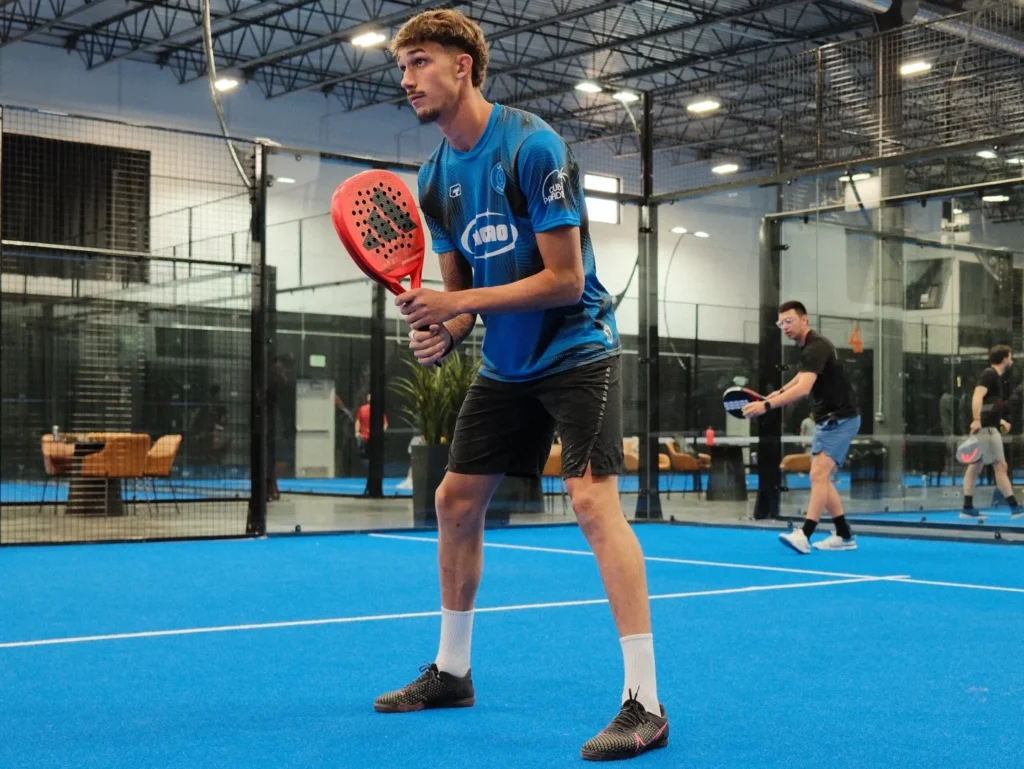 A male athlete getting ready to hit the ball on the premium blue indoor courts, bringing the global sport of padel to Orem.