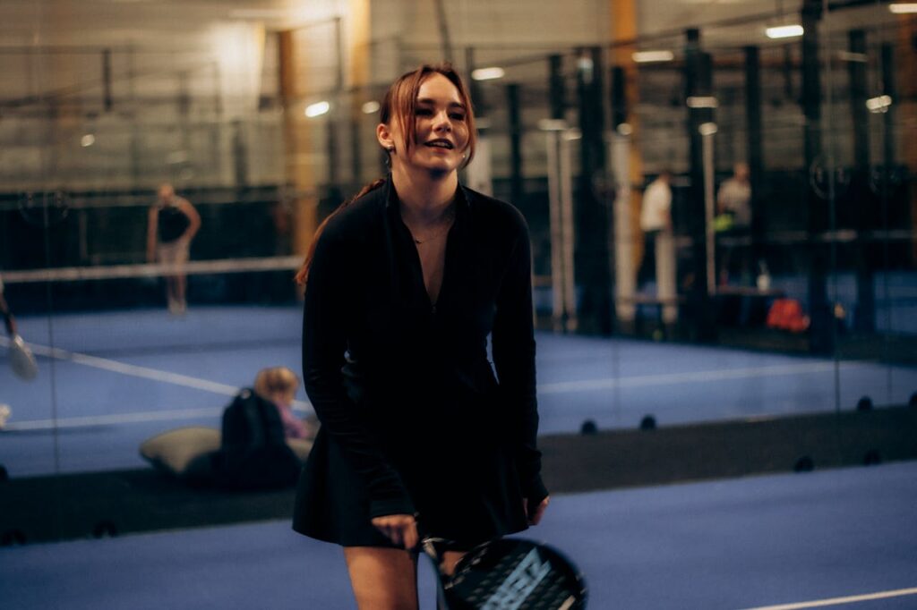 A female player smiling on the indoor blue court, demonstrating the social and mental health benefits of the sport.