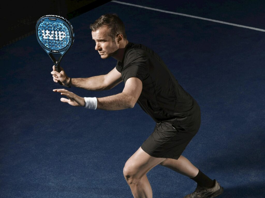 A male player in a low, intense athletic stance, instantly answering the question is padel a good workout.