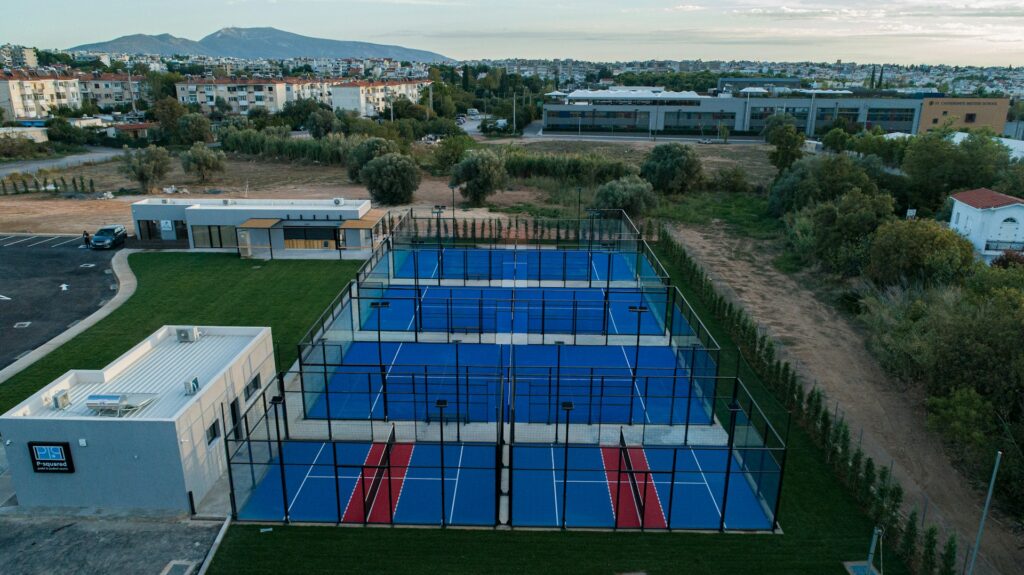 An aerial view of a large outdoor padel club with multiple blue courts, showcasing the global infrastructure required for Olympic inclusion.