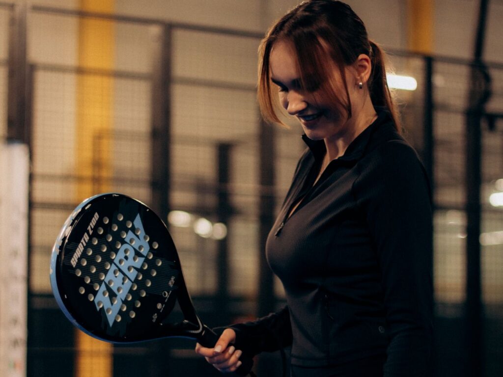A beginner player smiling and looking at her racket, practicing control over raw power on the court.