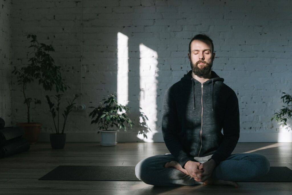 A man sitting cross-legged on a mat with his eyes closed, practicing mindfulness and deep breathing exercises for stress relief.