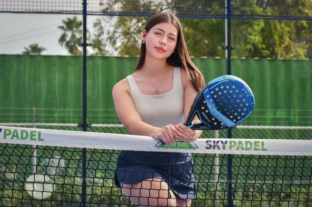 A female player leaning against the net tape holding a blue Kuikma racket, illustrating the net touch rule in padel.