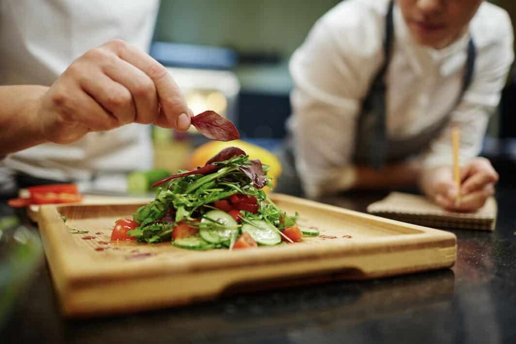 A chef carefully plating a fresh gourmet salad during an interactive corporate cooking class and team-building event.
