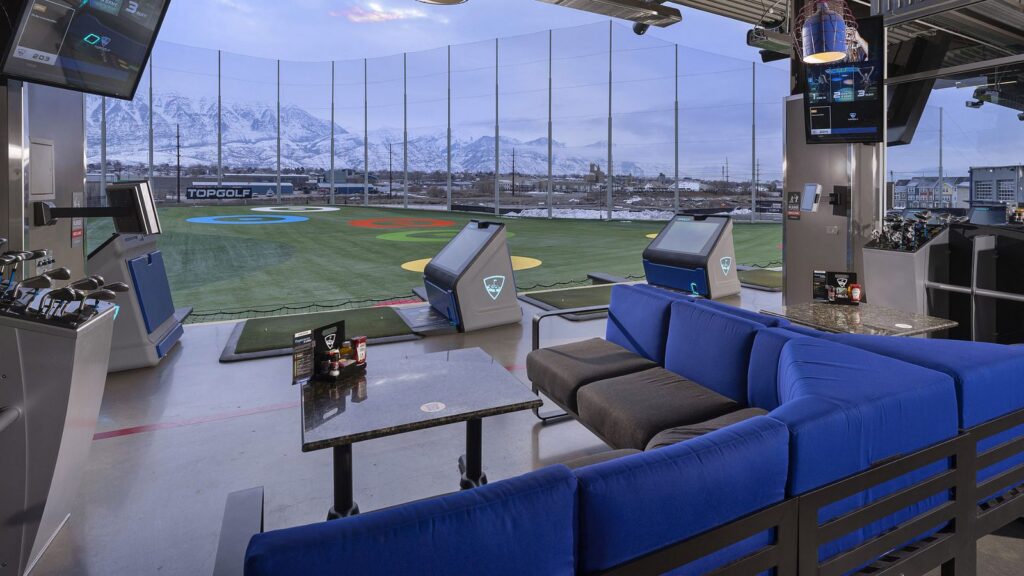 A climate-controlled hitting bay at Topgolf in Vineyard overlooking the driving range targets with the snowy Utah mountains in the background.