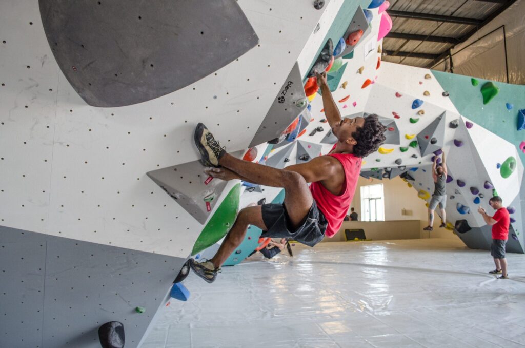 A man bouldering on an overhanging wall inside an indoor climbing gym, demonstrating an active team-building exercise.