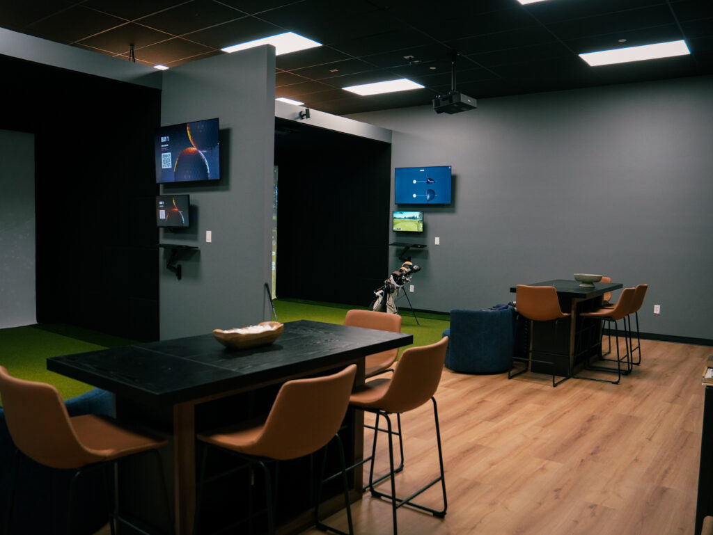 A sleek, private indoor golf simulator space at Player's Lounge Golf featuring modern high-top tables, lounge seating, and virtual hitting bays perfect for group events.