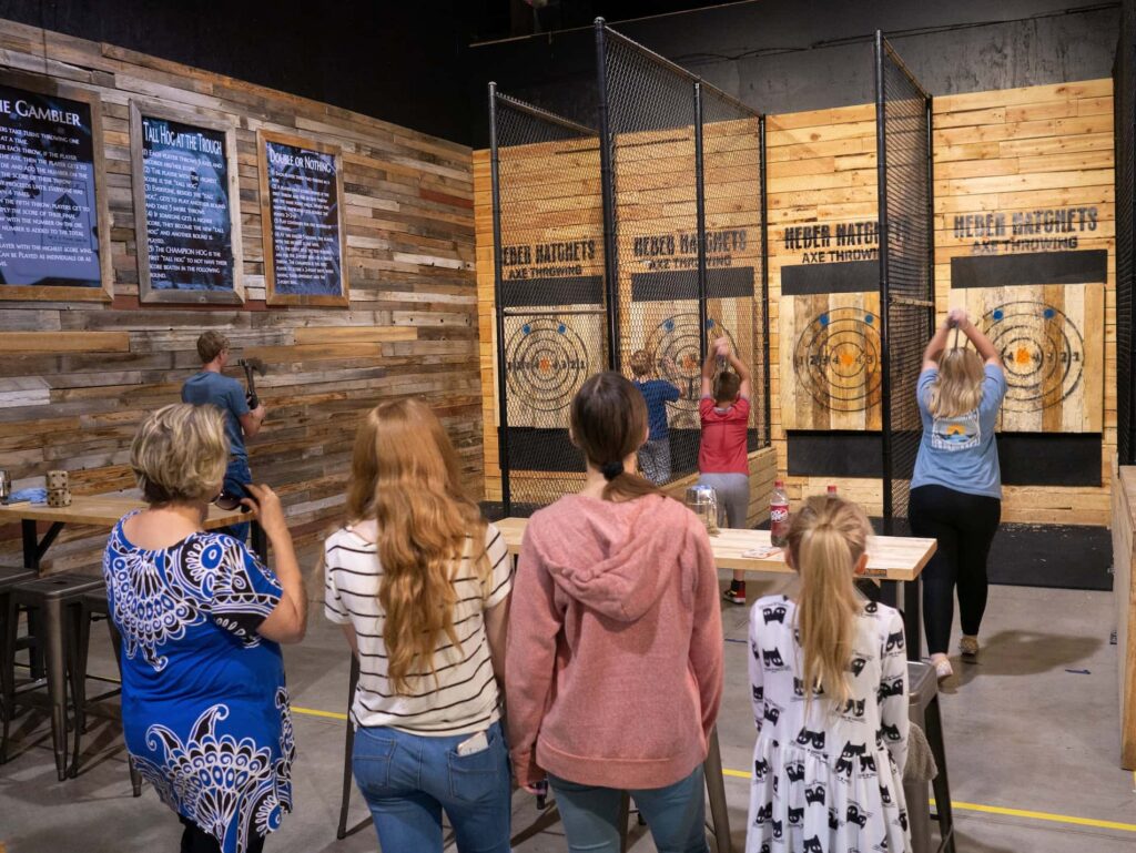A group of friends lined up in private indoor lanes throwing axes at wooden targets during a birthday party at Heber Hatchets.