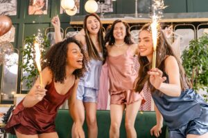 Four friends laughing, dancing, and holding sparklers together during an energetic girls' night out party.